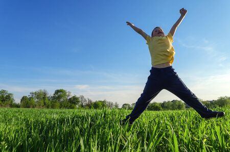 boy jumping on green meadow on the background of blue skyの写真素材