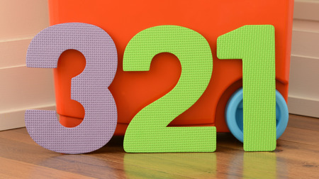 Colorful numbers 3,2,1 of flat foam toys on red plastic toy bin background and wooden floorの写真素材