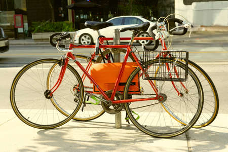Two red locked old road bikes with drop handlebars on circle metal bicycle rack on city street side walkの写真素材