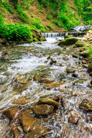 mountain river with stones and moss in the forest near the mountain slope horisontalの写真素材
