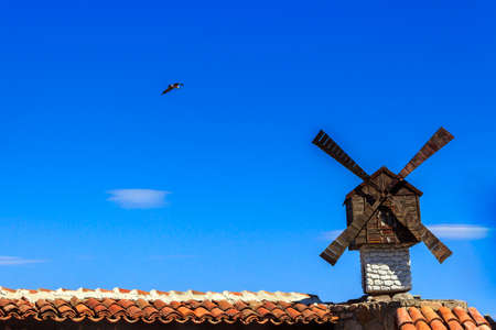 decorative windmill installed at the Architecture building on athe clear sky with a flying seagullの写真素材