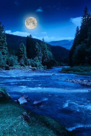river near embankment with trees at the mountain foot with fool moonの写真素材
