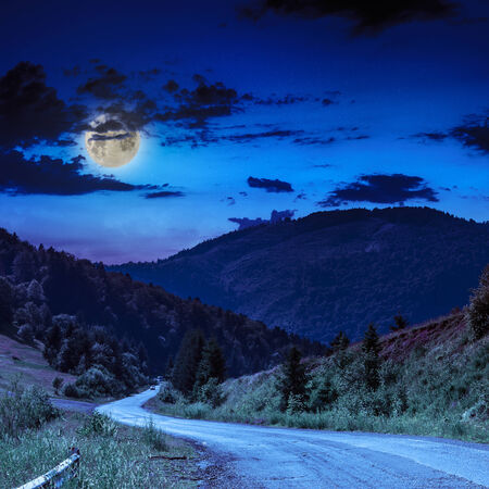 Empty asphalt mountain road with Painted single white Line near the coniferous forest with cloudy sky in moon lightの写真素材