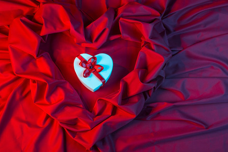love card. white heart with a red ribbon on a red fabric in blue lightの写真素材