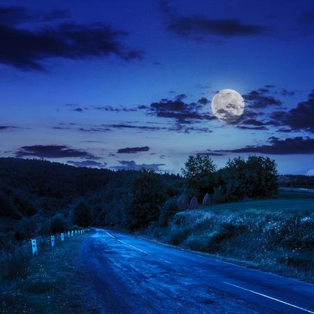 asphalt road going to mountain, passes rural places at night in moon lightの写真素材