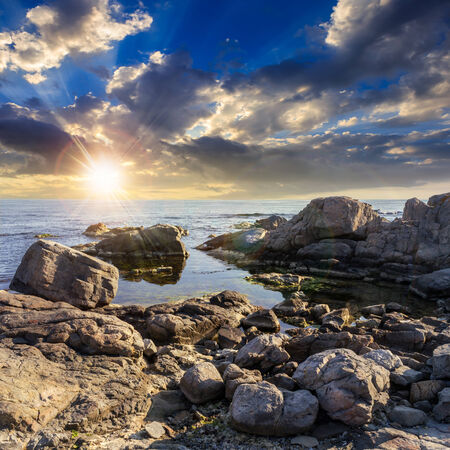 calm sea wave on rocky shore with boulders at sunsetの写真素材