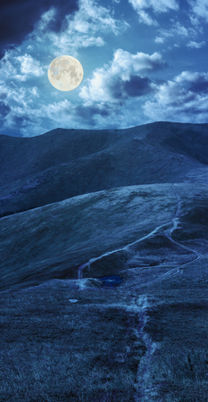 lake near the path in grass at the top of the mountain at night in full moon lightの写真素材