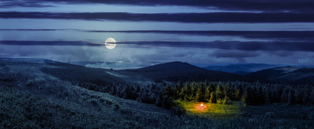 composite image of mountain range with bonfire in coniferous forest  on  hillside at night in full moon lightの写真素材