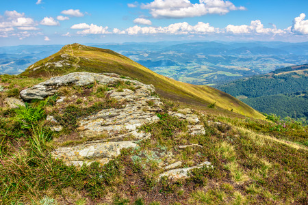 landscape with stones among the grass on the hillside near the path going to mountain top under a blue sky with cloudsの写真素材