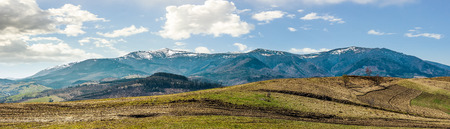 Early spring highland landscape. Panorama of rural fields on hill side in mountains with snowy peaksの写真素材