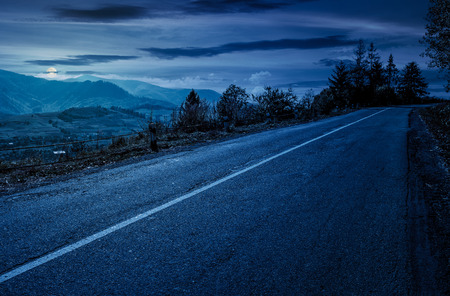 countryside road through mountains at night in full moon light. lovely autumnal sceneryの写真素材