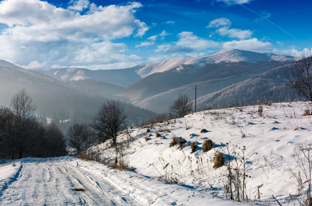 rural road in snowy mountainous area. beautiful winter scenery on a bright sunny day. mountains with...