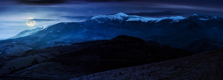 great mountain ridge Borzhava with snowy tops at night in full moon light. beautiful countryside landscape in late autumnの写真素材