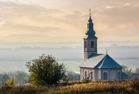 church on a hill over the hazy rural valley at sunset. lovely autumn countryside sceneryの写真素材