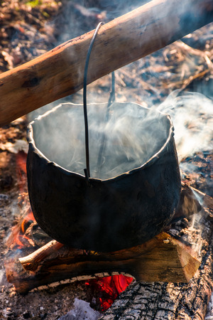 cauldron in steam and smoke on open fire. outdoor cooking concept. old fashioned way to make foodの写真素材