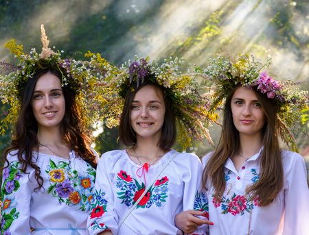Uzhgorod, Ukraine - 07 Jul, 2016: Portraits of three Young ladies with traditional wreath on their heads. background of park with light coming through smoke. Popular holiday in Slavic cultureのeditorial素材