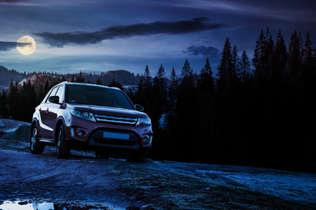 orange 4wd suv parked in mountain at night in full moon light. beautiful autumn scenery with gravel road through spruce forest. travel Europe by car conceptの写真素材