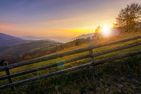 beautiful sunrise in mountains. countryside scenery in autumn. fence along the rural fields. distant mountains in hazeの写真素材