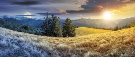 night and day time change concept above panorama of mountain landscape. beech trees on the meadow with weathered grass. svydovets ridge in the distance. clouds on a blue sky with sun and moonの写真素材