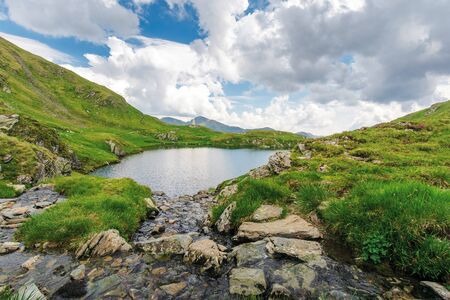 lake capra of romanian fagaras massif. beautiful alpine scenery of carpathians in summer. clouds on the blue sky. grass and boulders on the slopes. stream runs down the rocksの写真素材