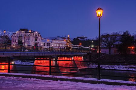 uzhgorod, ukraine - 06 JAN, 2019: winter dawn in town. wonderful urban scenery with city light on the bridge and christmas tree in the distance. lantern on the embankmentのeditorial素材