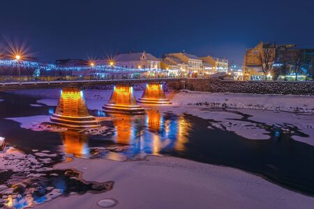 uzhgorod, ukraine - 06 JAN, 2019: winter dawn in town. wonderful urban scenery with city light on the bridge. lantern on the embankment. reflection on frozen waterのeditorial素材