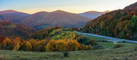 wonderful countryside in mountains at dusk.  serpentine road runs down in to the valley. trees on hills in colorful fall foliage. beautiful autumn panorama of carpathiansの写真素材