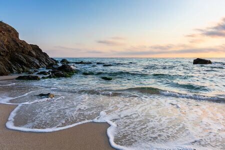sunrise on the beach. beautiful summer scenery. rocks on the sand. calm waves on the water. clouds on the sky. wide panoramic viewの写真素材