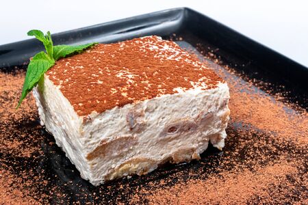 tiramisu cake on a black plate. tasty italian dessert decorated with mint