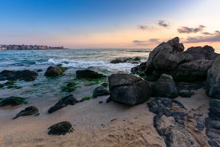 dramatic sunset on the sea shore. waves crashing rocks on sandy beach. beautiful cloudscape above...