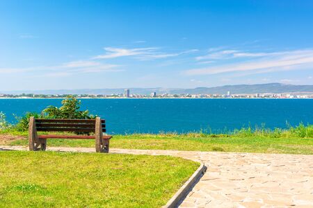 bench on the sunny beach shore. beautiful skyline view from empty park with paved footpath on the...
