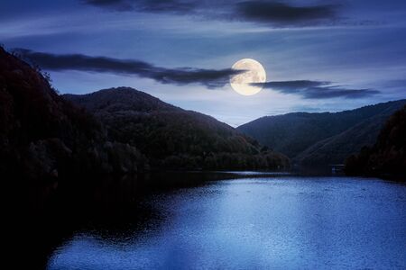 tarnita lake in romania at night. beautiful nature scenery in autumn in full moon light. gorgeous sky with glowing cloudsの写真素材