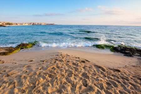 sandy beach with rocks. sunny morning in the resort town. wave brings seaweed on the stones on the shore. beautiful summer vacation landscape with clouds on the blue skyの写真素材