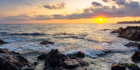 beach of the sea at sunset. wonderful scenery with stones in the water. beautiful clouds above the sun and horizon. concept of zen mood and spiritualityの写真素材