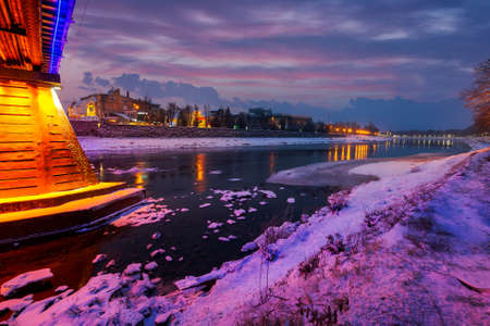 Uzhgorod, Ukraine - DEC 26, 2016: beautiful evening cityscape of old european town Uzhgorod in winter. wonderful cloudy sky over the river Uzh with some ice and snow on the shore. citylights reflect on the water surfaceのeditorial素材