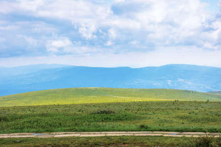 travel carpathian mountains in summer. road through green grassy meadows in the distance. idyllic landscape with clouds on the blue sky.の写真素材