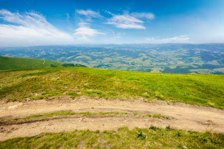 mountain road through grassy meadow. wonderful summer adventure. clouds on the blue skyの写真素材