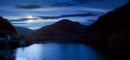 panorama of tarnita lake in romania at night. beautiful nature scenery in autumn in full moon light. gorgeous sky with glowing cloudsの写真素材