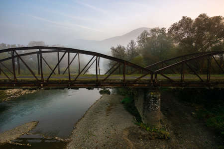 abandoned metal bridge in morning fog. dangerous construction in autumnal countryside scenery at sunriseの写真素材
