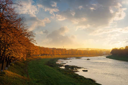 river uzh at sunrise. beautiful cityscape autumn scenery. linden alley in fall color in morning...