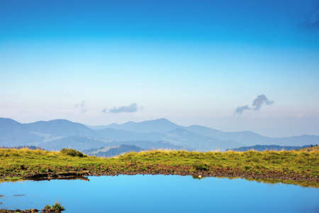 pond on the mountain meadow. beautiful summer landscape in morning light. grass on the hills. ridge in the distanceの写真素材
