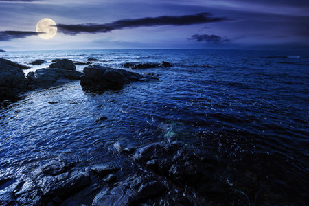sea coast scenery at night. boulders in the calm water. few clouds on the sky in full moon light. lonely place for summer vacations. sunny weatherの写真素材