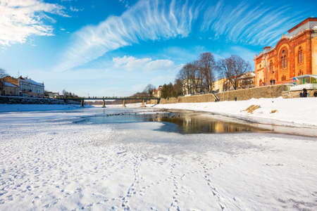 uzhgorod, ukraine - JAN 09, 2017: winter holidays in old town. embankment in snow and river uzh covered with ice. red building of old synagogueのeditorial素材
