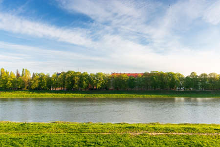 embankment of the river uzh in morning light. grassy shore and linden alley in spring season. travel ukraine concept. blue sky with cloudsの写真素材