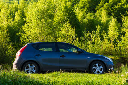 turya, ukraine - MAY 17, 2021: small hatchback in outdoor nature scenery. car on the countryside road through meadow. trees on the near by hill. beautiful springtime landscape in morning lightのeditorial素材