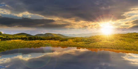 landscape with lake in summer at sunset. peaceful reflection in the water. beautiful travel view in chernohora ridge, ukraine. tranquil nature background in evening light. green outdoor sceneryの写真素材