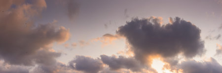 panorama of a sky in warm evening light. massive clouds in orange color at sunsetの写真素材