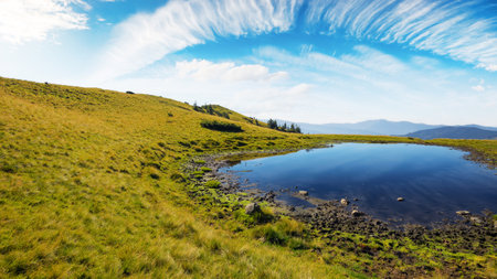 pond in mountains. beautiful countryside landscape of transcarpathia. clouds above horizon on a warm sunny dayの写真素材