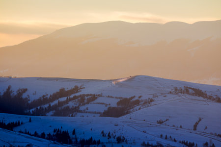 mountainous countryside scenery in winter at sunrise. landscape with rural fields on the snow...
