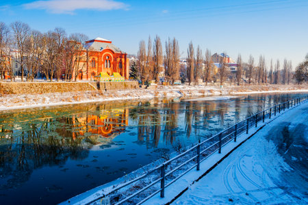 uzhgorod cityscape in winter. urban landscape with snow covered embankment. red building of a former...
